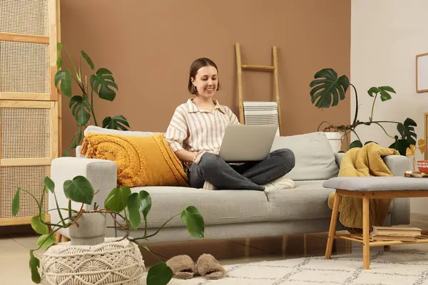 Oturma odasındaki kanepede dizüstü bilgisayarla çalışan genç bir kadın.