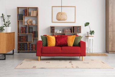 Beyaz duvarın yanında kırmızı kanepe ve kitaplık olan oturma odasının içinde.