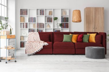 Beyaz duvarın yanında kırmızı kanepe ve kitaplık olan oturma odasının içinde.