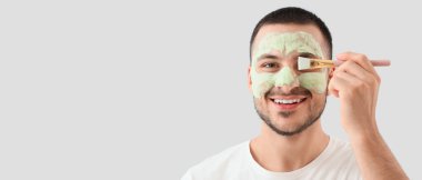 Yüzünde kozmetik balon maskesi ve gri arka planda fırçası olan yakışıklı genç adam.