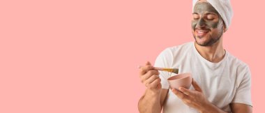 Yüzünde kozmetik kil maskesi olan yakışıklı genç adam pembe arka planda.