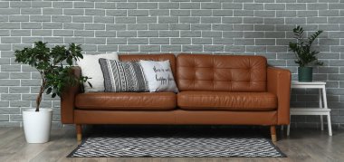 Yumuşak yastıklı kahverengi deri kanepe ve oturma odasındaki gri tuğla duvarın yanında bitkiler.