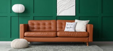 Yumuşak yastıklı kahverengi deri kanepe ve oturma odasındaki yeşil duvarın yanında yer lambası