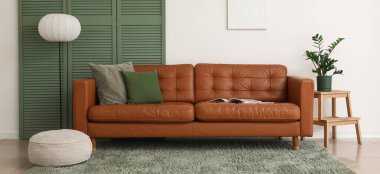 Kahverengi deri kanepe, yumuşak puf ve beyaz duvarın yanındaki oturma odası.