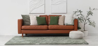 Yumuşak yastıklı kahverengi deri kanepe ve oturma odasındaki beyaz duvarın yanında puf.