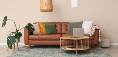 Kahverengi deri kanepe ve oturma odasındaki bej duvarın yanında modern dizüstü bilgisayarı olan ahşap masa.