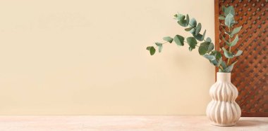 Bej arkaplan üzerinde yeşil okaliptüs dalları ve metin için alanı olan vazo