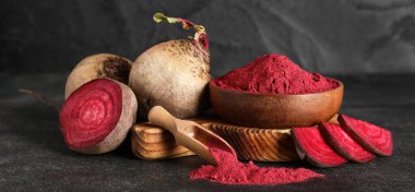 Ahşap bir kase canlı pancar tozu kepçeli ve siyah arka planda taze pancarlar.