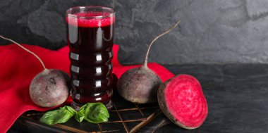 Siyah arka planda fesleğenli ve sebzeli bir bardak taze pancar suyu.