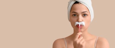 Yüzünde jilet ve tıraş köpüğü olan genç bir kadın bej arka planda ve mesaj için yeri var. Saç çıkarma konsepti