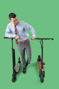 Handsome businessman with kick scooters on green background