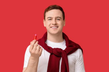 Kırmızı arka planda dudak merhemi olan mutlu genç adam.