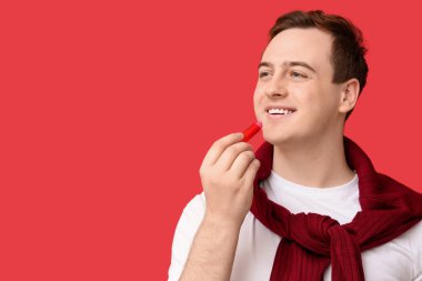 Kırmızı arka plana dudak kremi süren yakışıklı genç adam.