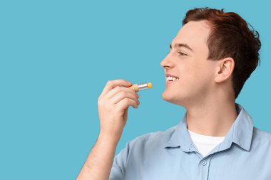 Yakışıklı genç adam mavi arka plana dudak kremi sürüyor.