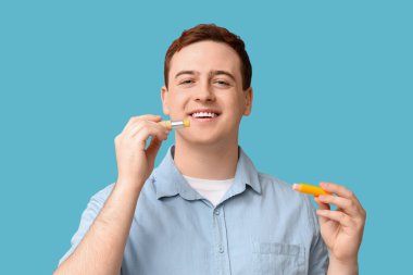 Mavi arka planda dudak kremi olan yakışıklı bir genç.