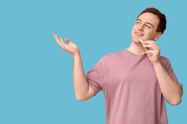 Dudak merhemi ile yakışıklı genç adam mavi arka plandaki bir şeyi işaret ediyor.