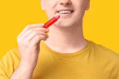 Sarı arka planda dudak kremi süren genç adam, yakın plan.