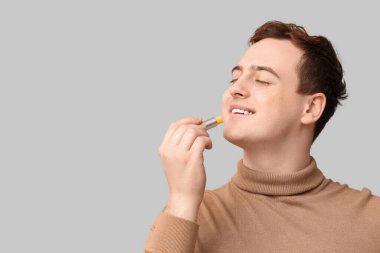 Gri arka plana dudak kremi süren yakışıklı genç adam.