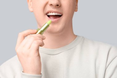 Gri arkaplanda dudak kremi olan genç bir adam.