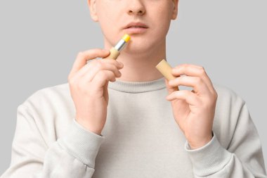 Gri arka plana dudak kremi süren genç bir adam.