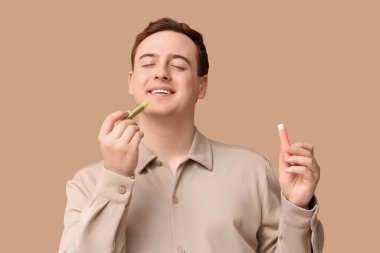 Kahverengi arka planda dudak kremi olan yakışıklı bir genç.