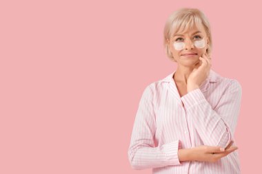 Pembe arka planda göz altı yamaları olan pijamalı güzel, olgun bir kadın.