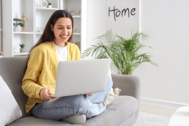 Evdeki kanepede dizüstü bilgisayarla sohbet eden güzel bir genç kadın.