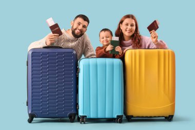 Mavi arka planda pasaportları ve bavulları olan mutlu bir aile. Seyahat kavramı