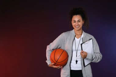 Siyah arka planda top ve panosu olan Afro-Amerikan bayan basketbol antrenörü.