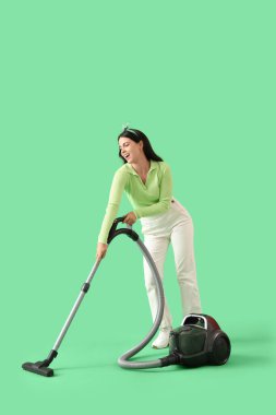 Yeşil arka planda elektrik süpürgesi olan genç bir kadın.