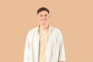 Bej arka planda gülümseyen tişörtlü genç adam.