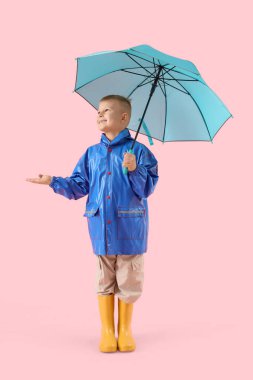 Pembe arka planda şemsiyesi olan yağmurluk giymiş şirin bir çocuk.