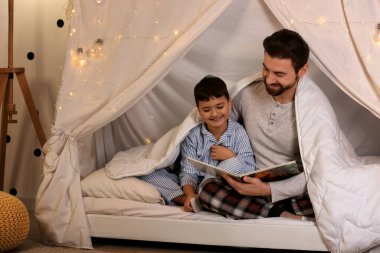 Baba ve küçük oğlu battaniyeyle kulübede masal okuyorlar.