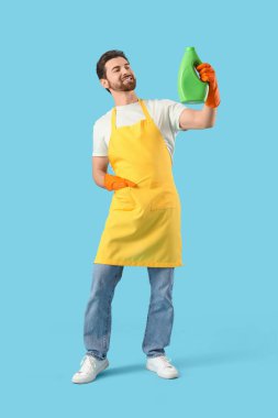 Önlüklü yakışıklı, mavi arka planda çamaşır deterjanı var.