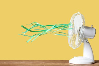 Sarı arka planda yeşil dalgalı kurdeleleri olan modern elektrikli vantilatör.