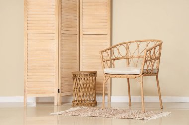 Hasır sandalye, kahve masası ve odada bej duvarın yanında katlanan ekran.