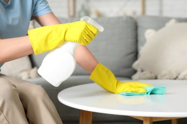 Oturma odasında bez parçasıyla masayı temizleyen genç bir kadın. Yakın çekim.