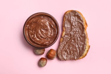 Çikolatalı ekmek dilimi ve pembe arka planda fındıklar.