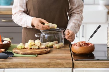 Mutfaktaki tencereye lahana dolması koyan kadın, yakın plan.