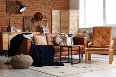 Oturma odasının içinde deri kanepe, koltuk, katlanır ekran ve kahve masası.