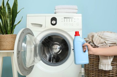 Çamaşır odasında çamaşır makinesinin yanında bir şişe deterjanı olan bir kadın.