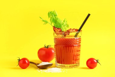 Sarı arka planda domuz pastırması ve kereviz ile bir bardak Bloody Mary kokteyli.