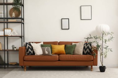 Yumuşak yastıklı kahverengi deri kanepe ve oturma odasındaki beyaz duvarın yanında modern laptop.