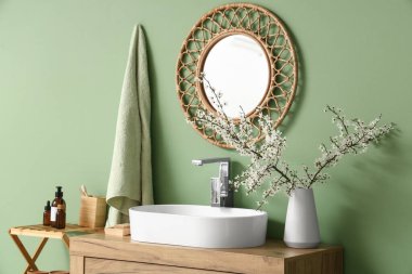 Çiçek açan dallarla dolu vazo ve banyoda yeşil duvarın yanındaki çekmecelerin üzerine lavabo, yakın plan.