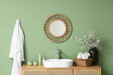 Banyodaki yeşil duvarın yanındaki çekmecelerde çiçek açan dallar ve banyo malzemeleri olan vazo.