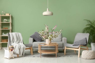 Koltuklu kanepe, sehpa ve oturma odasındaki yeşil duvarın yanında açan dallardan oluşan vazo.