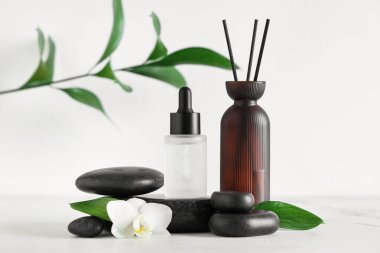 Temel yağ şişesi, sazlık dağıtıcı ve hafif arka planda spa taşlarıyla bileşim