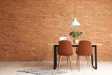 Laptoplu yemek masası ve odada tuğla duvarın yanına bitki.