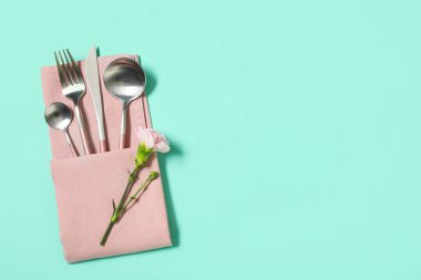 Gümüş çatal bıçak takımı ve turkuaz arka planda karanfil çiçeği.