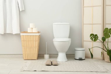 Seramik klozet, çöp kutusu ve sepeti olan şık bir tuvalet.